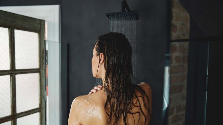 Dunkelhaarige Frau mit nassen Haaren in der Dusche. Ansicht von hinten.