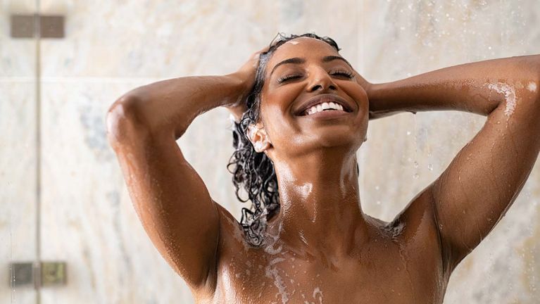 Femme riant sous la douche. La tête penchée en arrière et se savonnant les cheveux.