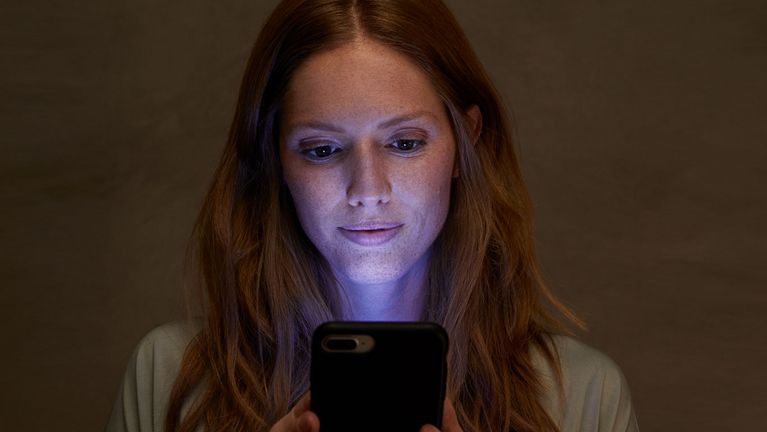 De jonge vrouw bekijkt mobiele telefoon met het scherm dat kunstmatig blauw licht uitzendt