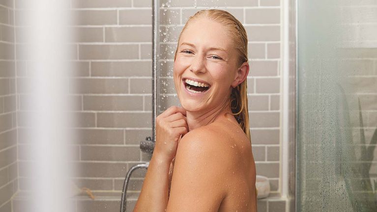 Blonde Frau lachend unter der Dusche.